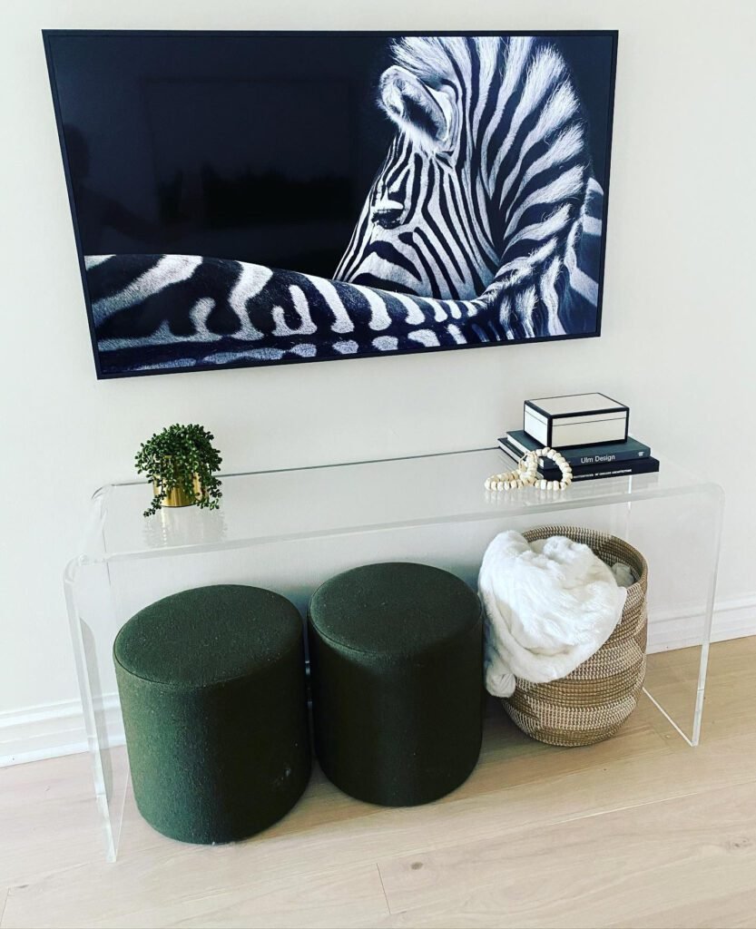 Clear acrylic console table beside TV with vintage-inspired decor.