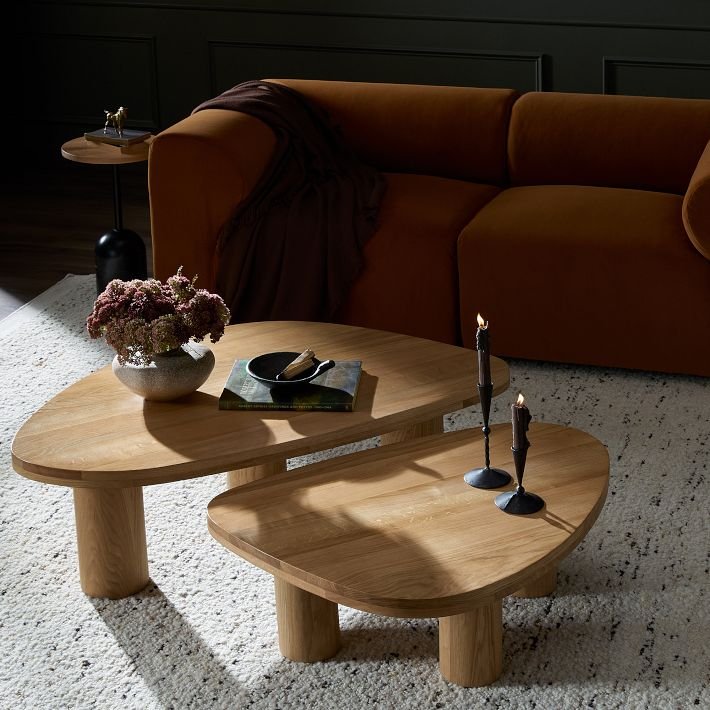 Two overlapping wooden nesting tables with curved edges, set in a warm-toned living room.
