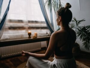 Woman meditating by a sunlit window with soft curtains.