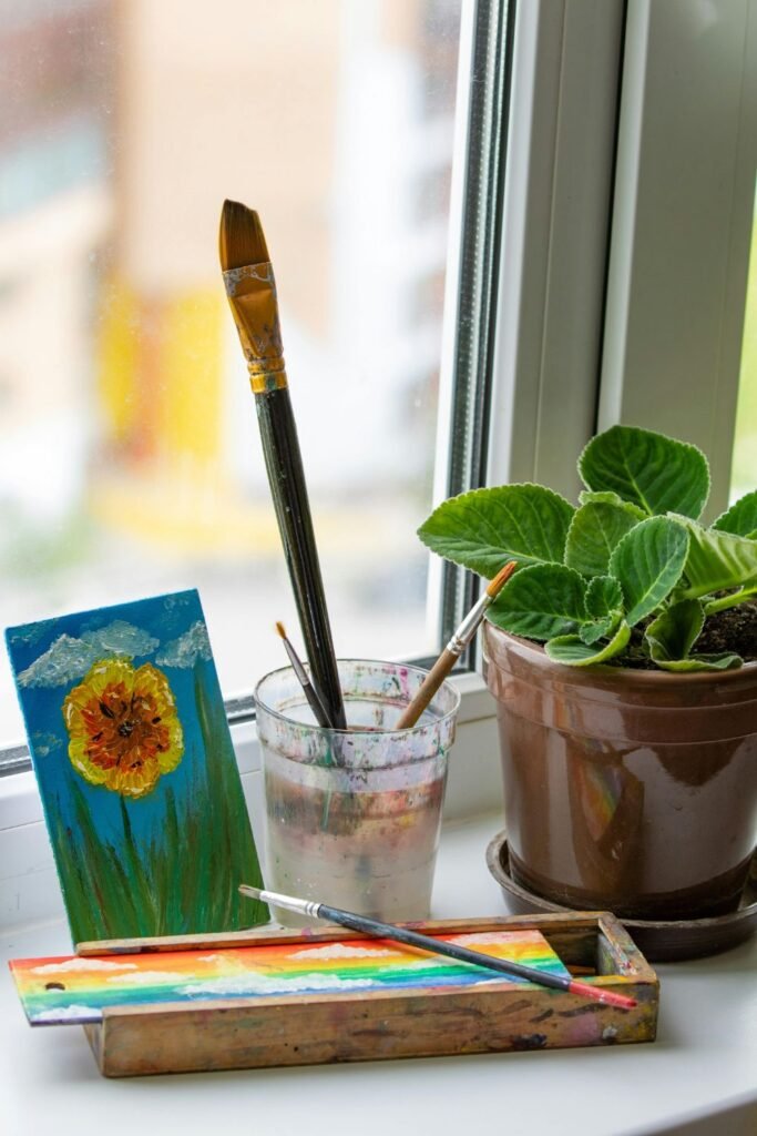Watercolor paints and brushes beside a potted plant on window ledge