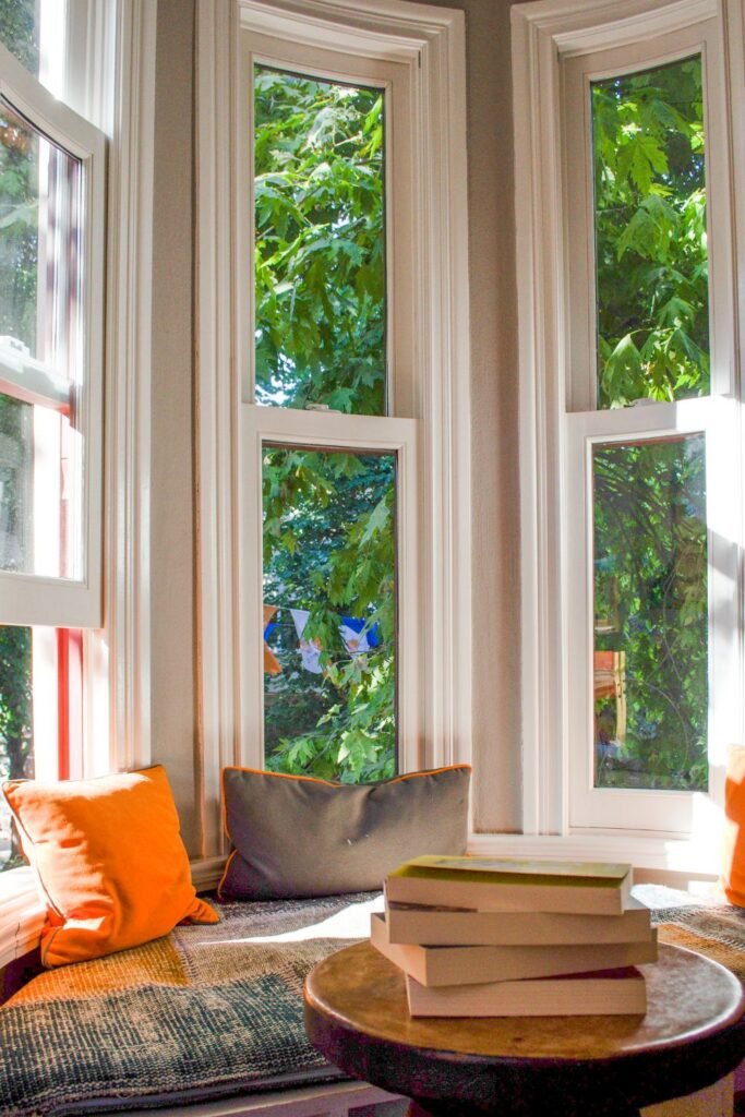 Sunlit window nook with cushions, books, and cozy seating for reading.