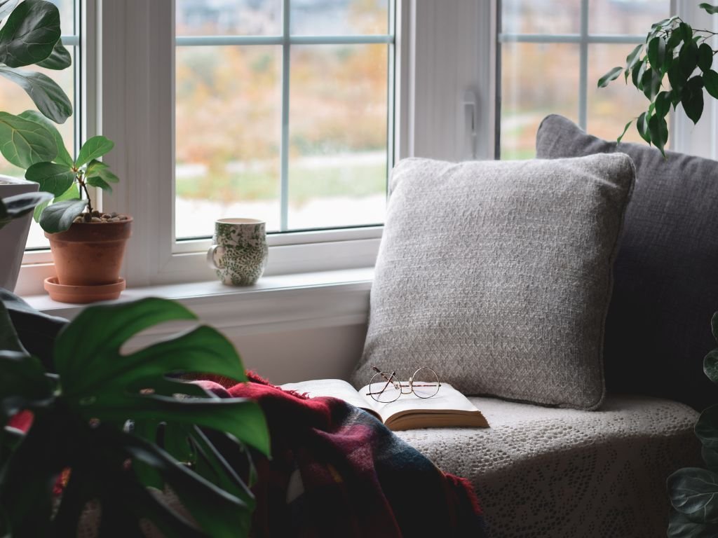 Cozy window nook with chair, pillows, and plants creating a bright spot for reading.