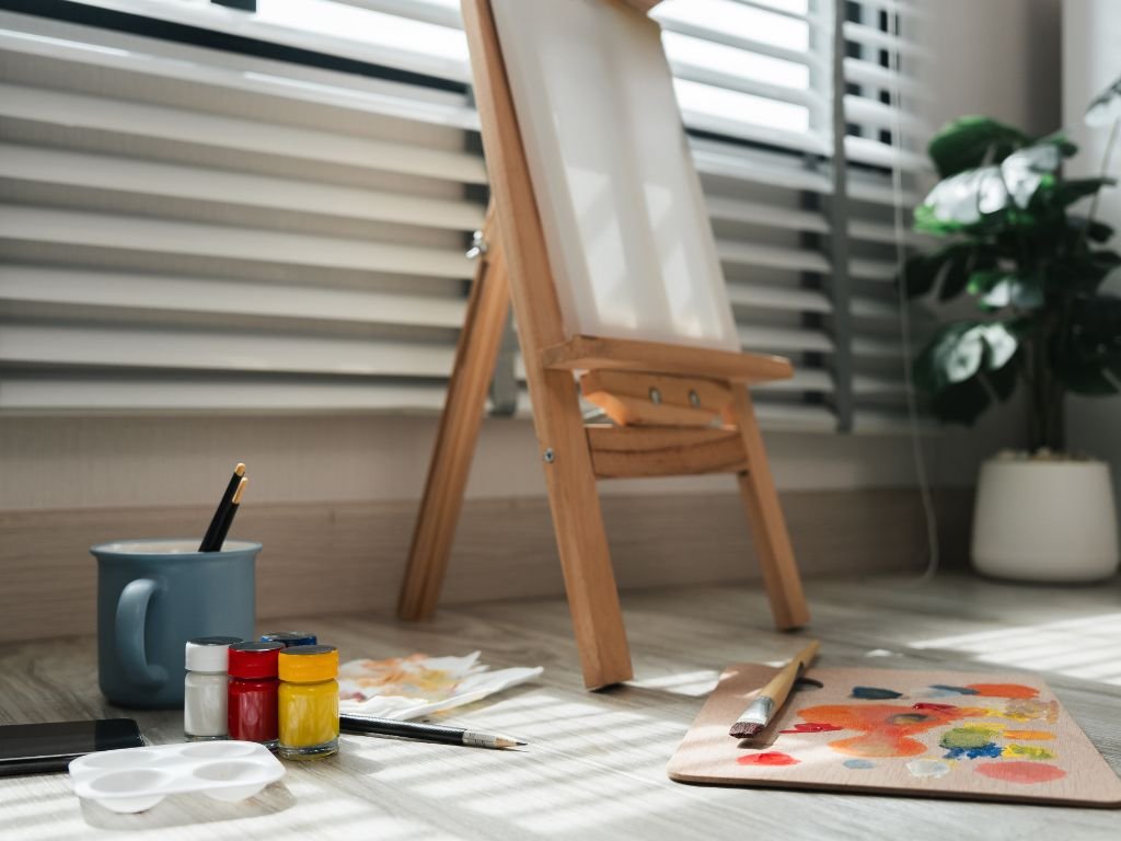 Easel and paints set up by a sunny window.