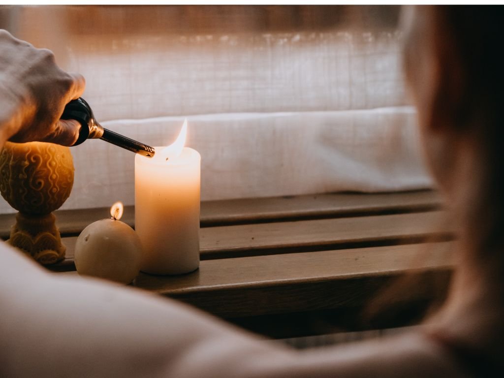 Close-up of a candle burning near a cozy window ledge.