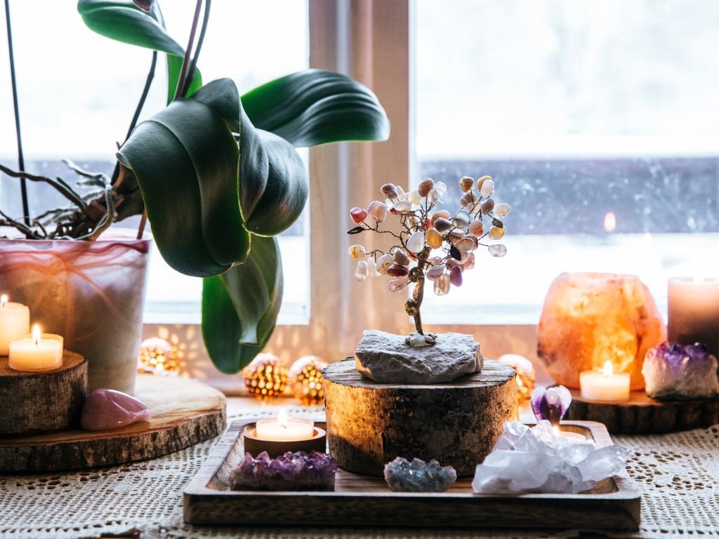 Assortment of glowing candles and plants by window.