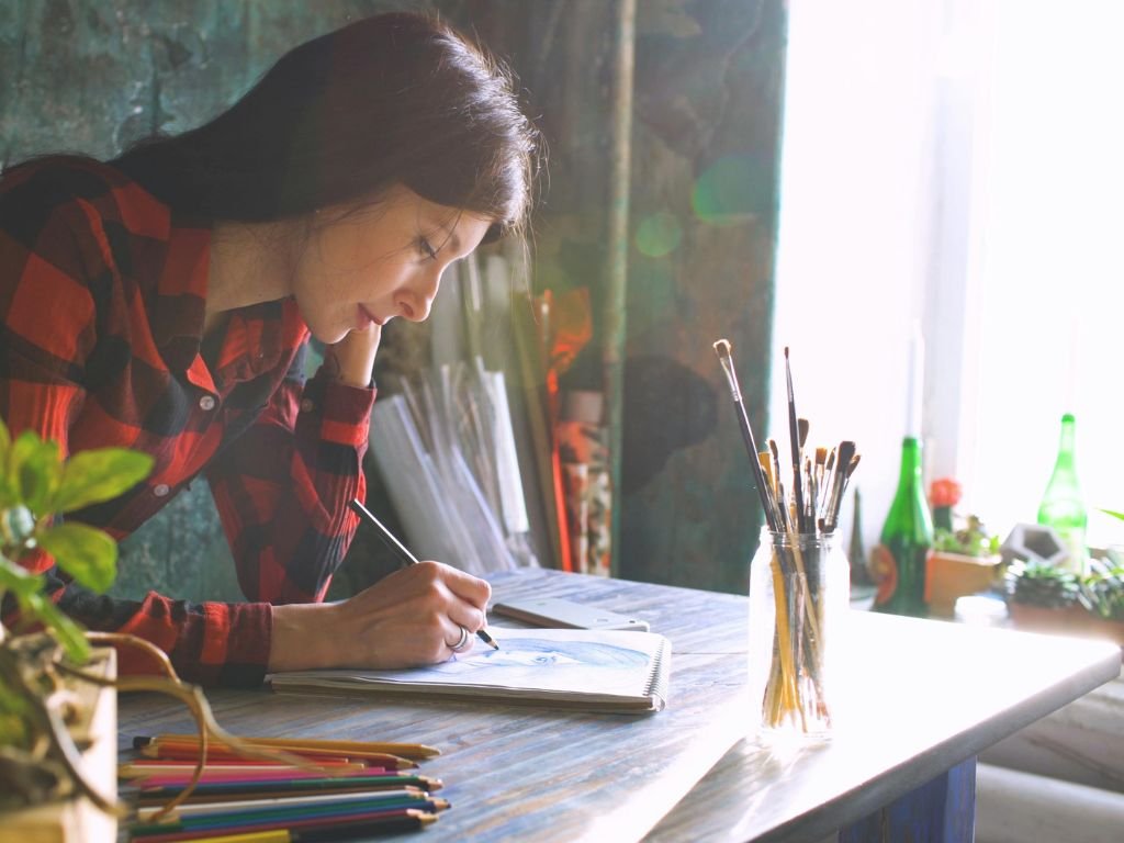 Person sketching at a window desk with plants.